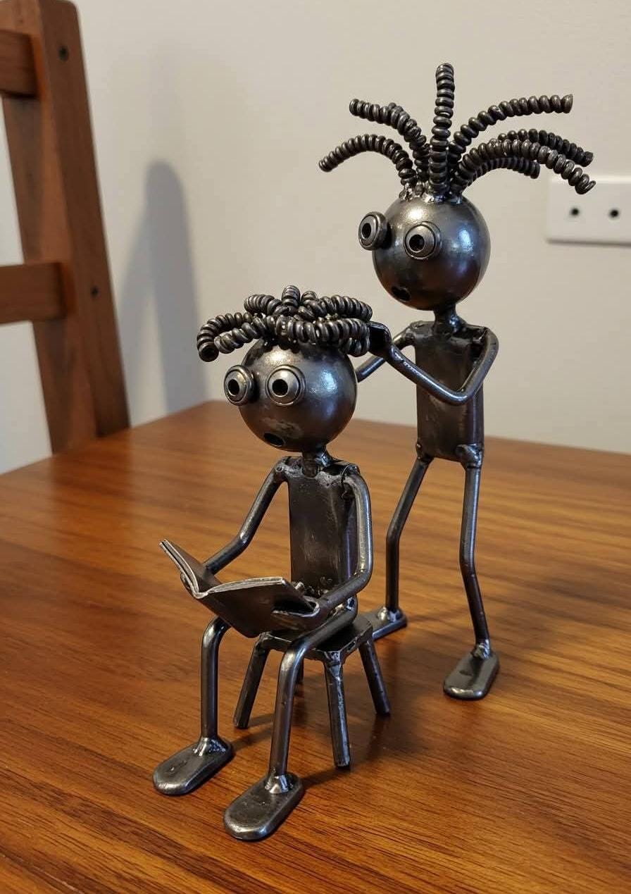 Pair of metal figures, one seated with a book and one standing nearby.