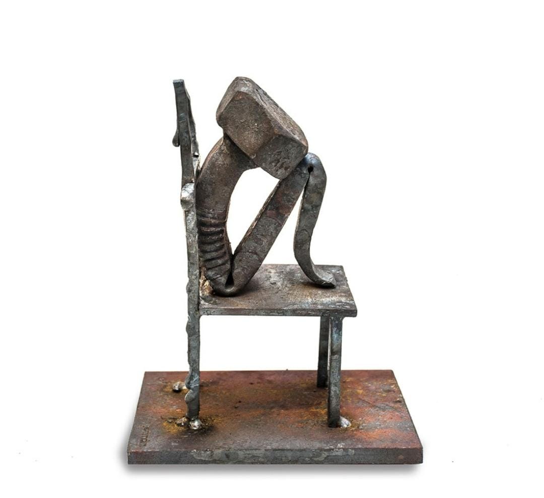Abstract metal figure seated on a chair-shaped metal sculpture.