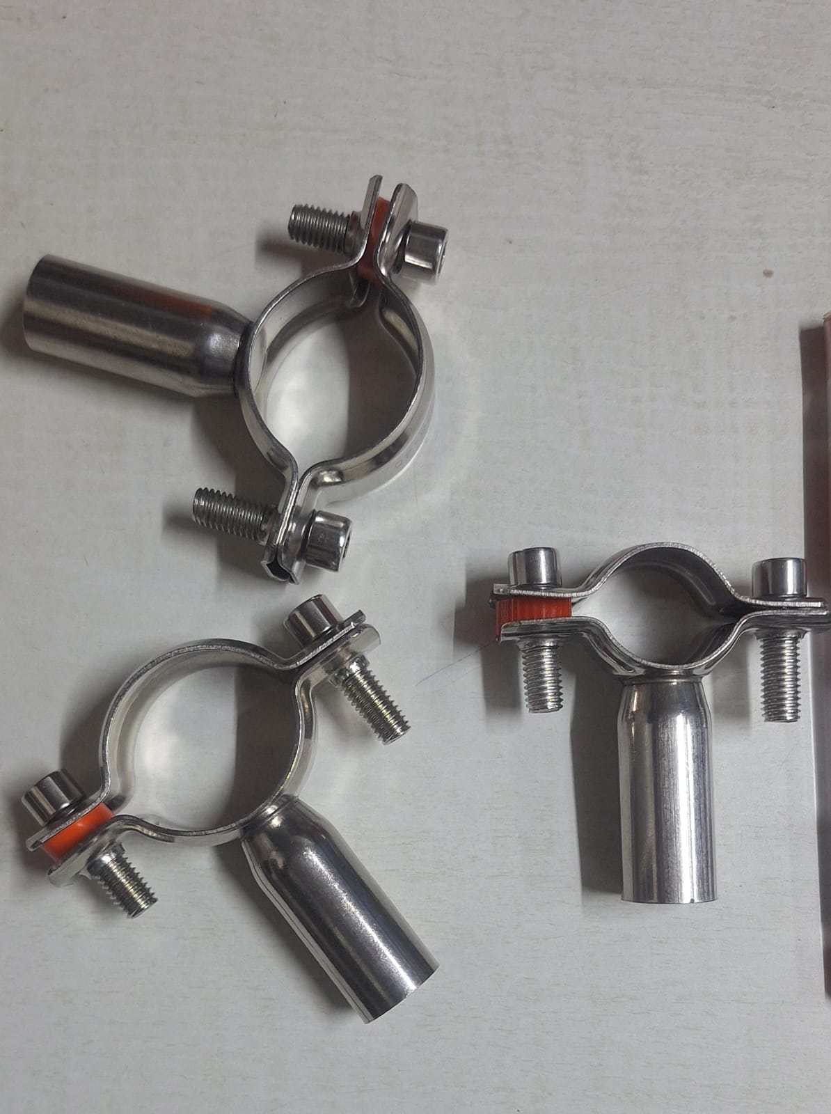 Three metal pipe holder clamps arranged on a light surface.