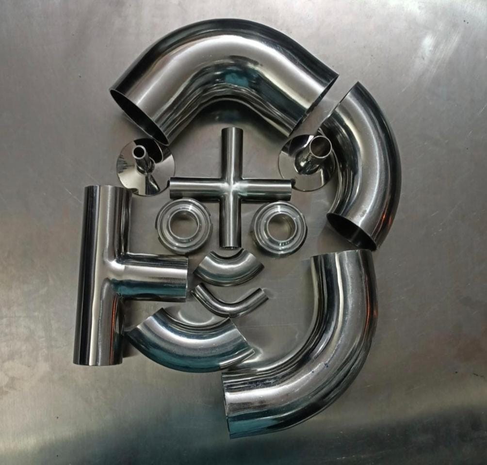 Polished metal bend and tee fitting components arranged on a work surface.