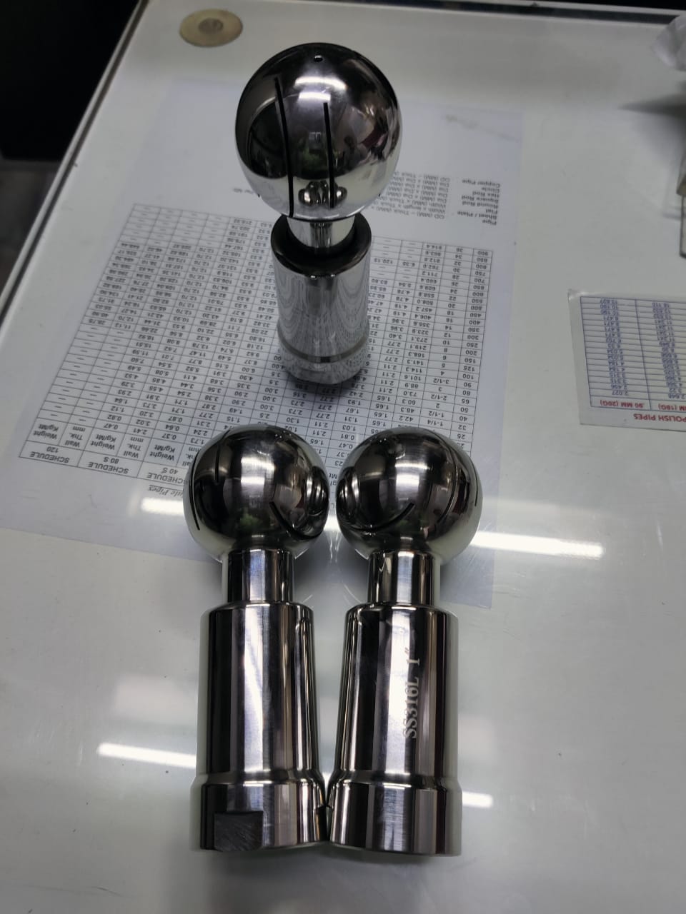 Three polished stainless steel rotary spray ball assemblies arranged on a light surface.