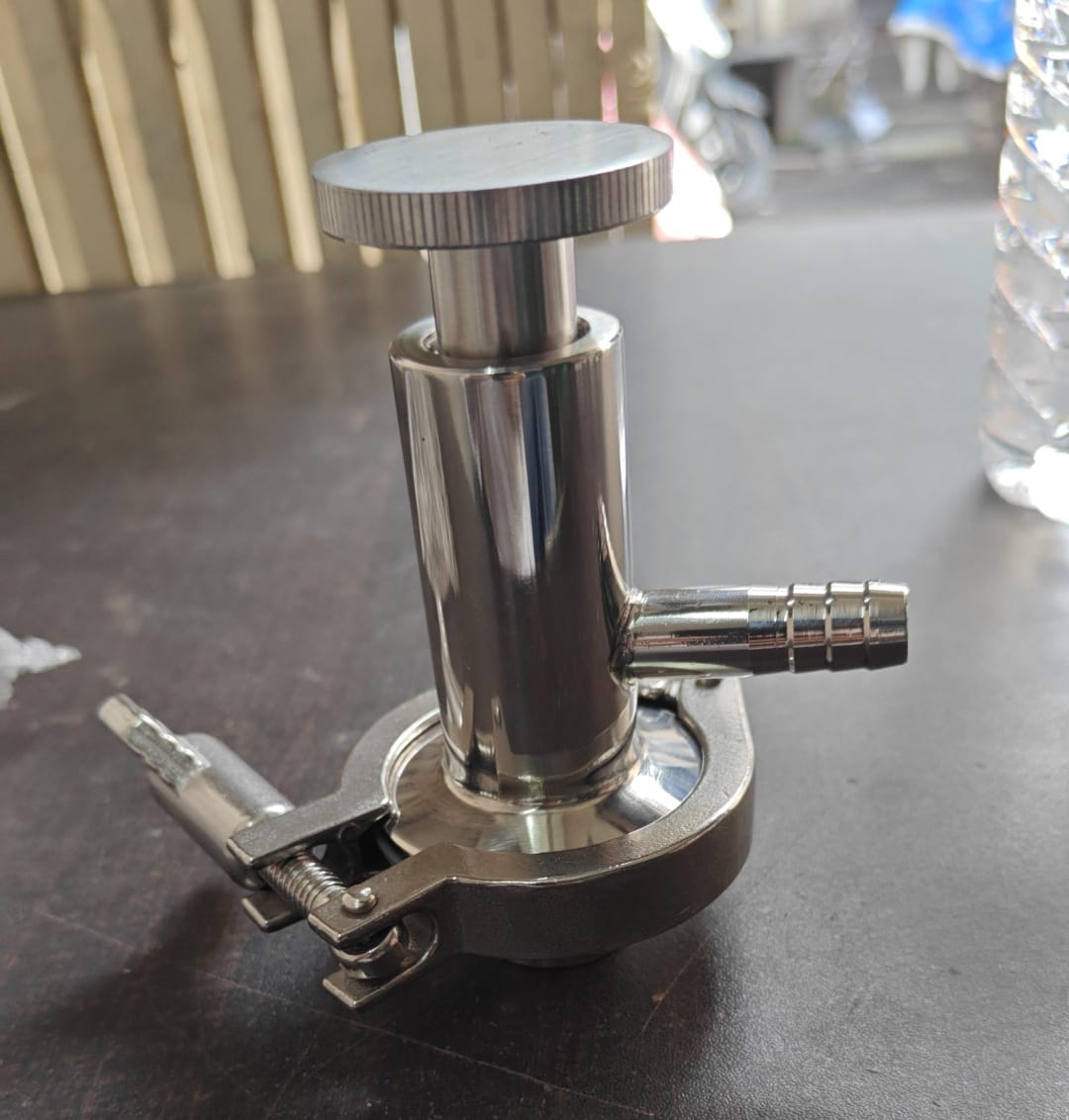 Polished stainless steel sampling cock with a top handle, side hose barb and sanitary clamp base.