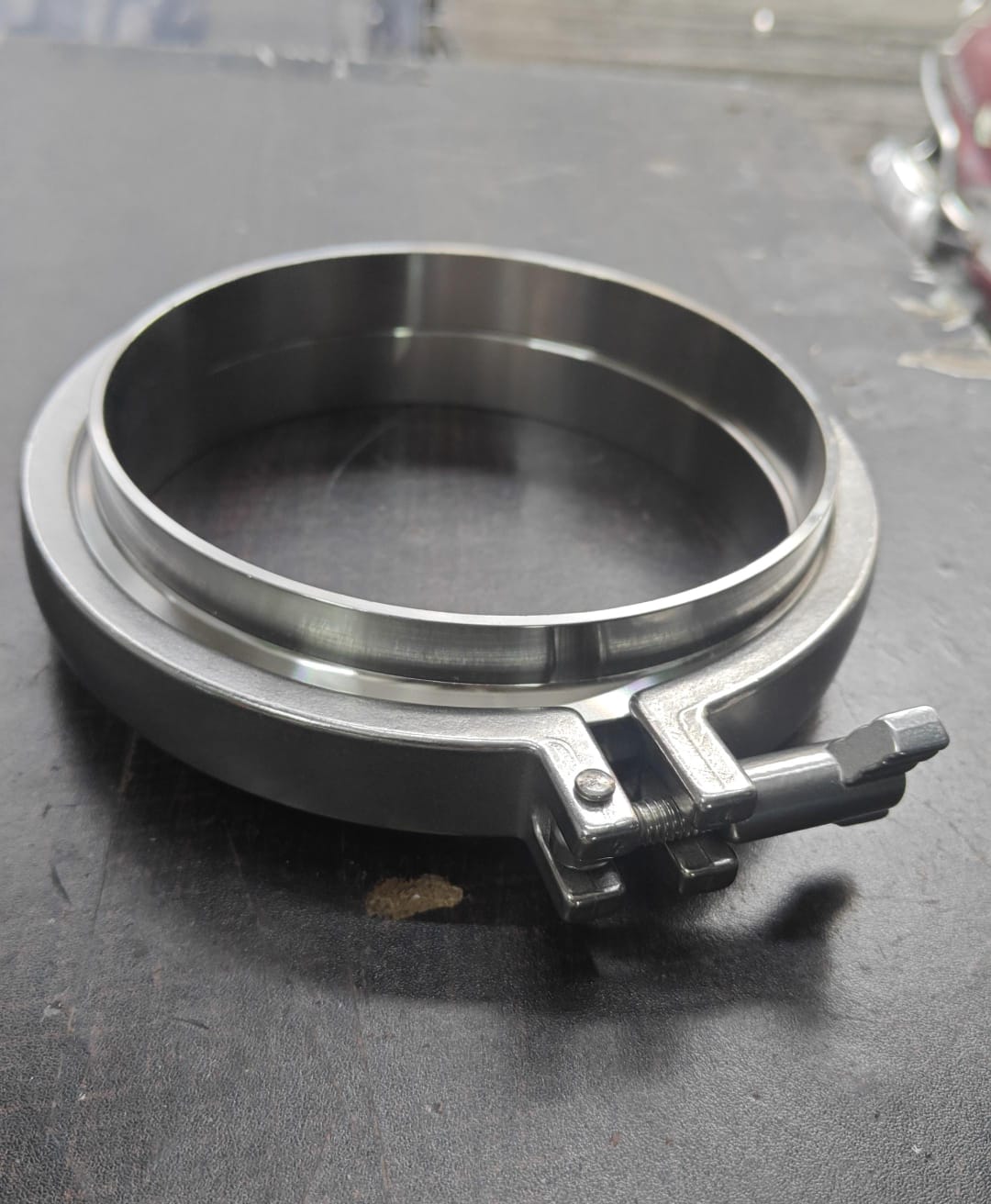 Polished stainless steel sanitary clamp with a circular ring and hinged lever lock.