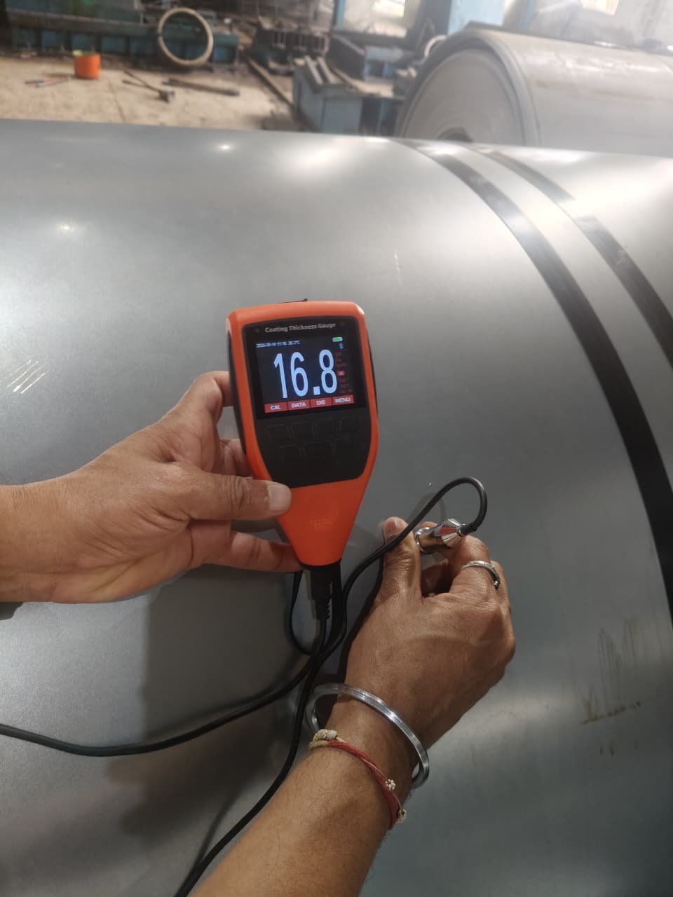 Coating thickness gauge testing a coated steel pipe surface in the warehouse